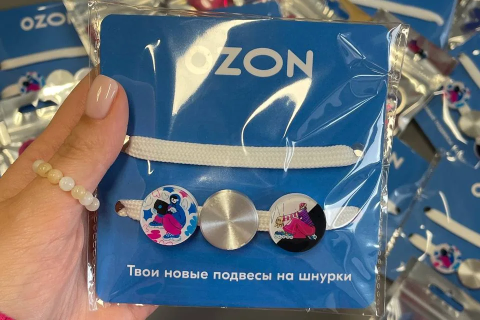 Подвесы на шнурки в синей фирменной упаковке Ozon в руке, на фоне — тираж таких же